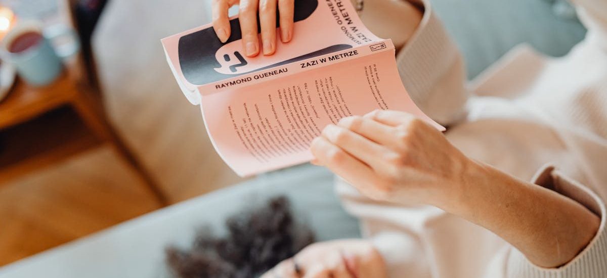 A woman is relaxing indoors while lying down and reading a book, creating a cozy atmosphere.