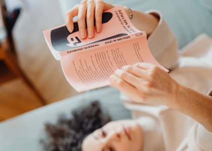 A woman is relaxing indoors while lying down and reading a book, creating a cozy atmosphere.