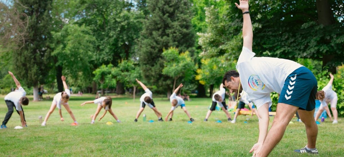 Kids stretching exercises in a park guided by a coach, promoting fitness and fun.